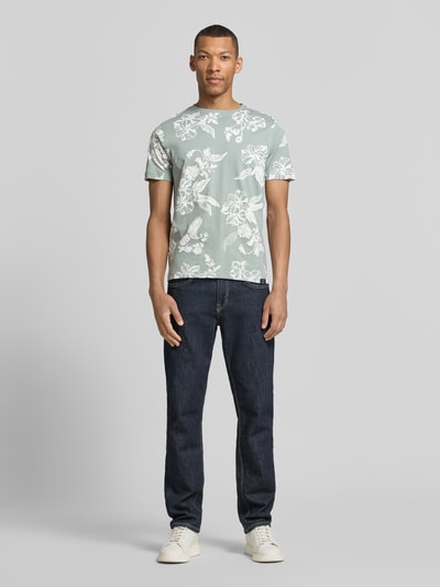 Męski model nosi T-Shirt mit Rundhalsausschnitt und Label-Detail od Lerros, czysta bawełna, krój regular fit, długość tyłu w rozmiarze M: 70 cm, jasnoszary z białym wzorem kwiatowym, gładka tekstura, widok całej sylwetki z przodu.