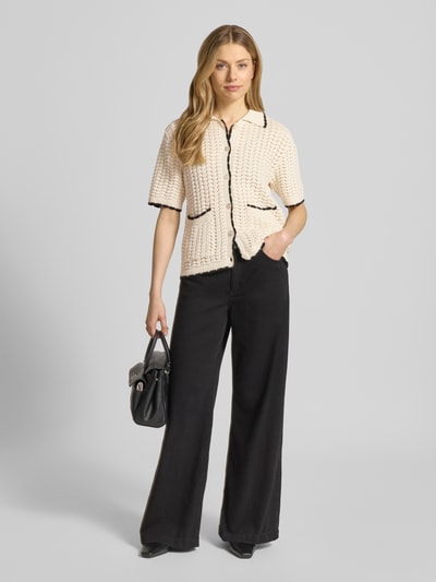 Frauenmodel trägt Regular Fit Cardigan mit Lochmuster Modell 'Muno' von B.Young aus reiner Baumwolle in Strick-Optik, Schwarz und Creme, kurzärmelig, Umlegekragen, aufgesetzte Taschen, durchgehende Knopfleiste, Ganzkörperansicht von vorne.