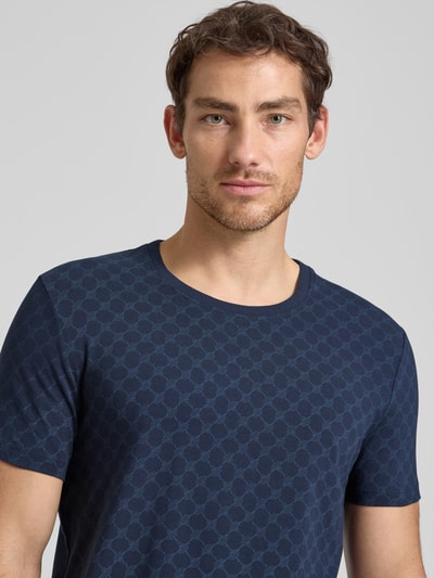 Männermodel trägt T-Shirt mit Logo-Muster und Rundhalsausschnitt von JOOP! Collection aus Baumwoll-Elasthan-Mix, Regular-Fit, Nahaufnahme Oberkörper.