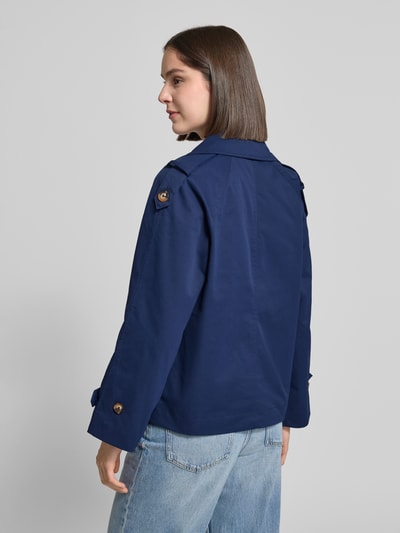 Kobiece model nosi trencz Trenchcoat mit Ärmelriegeln Modell 'AMONA' od B.Young, krój regular fit, dwurzędowy, wykładany kołnierz, wpuszczane kieszenie, patki przy mankietach, długość tyłu w rozmiarze 36: 63 cm, szerokość ramion w rozmiarze 36: 46 cm, szerokość klatki piersiowej w rozmiarze 36: 52 cm, długość rękawów w rozmiarze 36: 46 cm, kolor granatowy, gładka tekstura, widok całej sylwetki z tyłu.