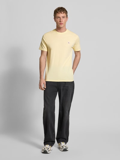 Männermodel trägt T-Shirt mit Label-Badge von Calvin Klein Jeans in Gelb, reine Baumwolle, Regular-Fit, Rundhalsausschnitt, Ganzkörperansicht von vorne. Rückenlänge bei Größe M 70 cm.