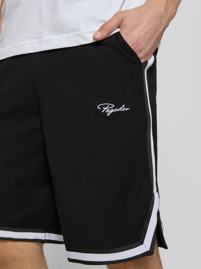 Männermodel trägt Shorts mit Logo-Stitching Modell 'Signar' von Pegador in Schwarz mit weißen Kontraststreifen, Reine Baumwolle, Gerader-Schnitt, Nahaufnahme Oberschenkel.