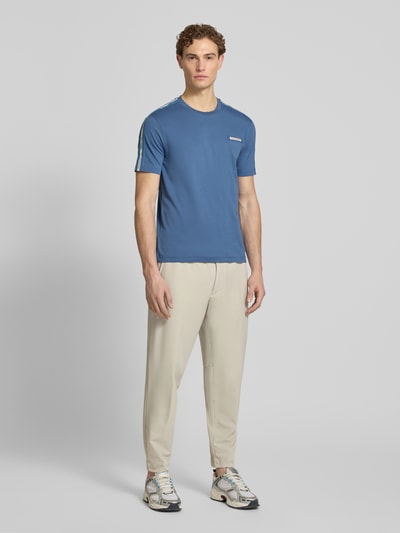 Männermodel trägt T-Shirt mit Label-Patch und Rundhalsausschnitt von EA7 Emporio Armani in Blau, körpernah, reine Baumwolle, Ganzkörperansicht von vorne.