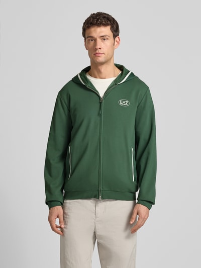 Męski model nosi Sweatjacke mit Logo und Zweiwege-Reißverschluss od EA7 Emporio Armani, zieleń, kaptur, regular fit, widok z przodu, całe ciało.
