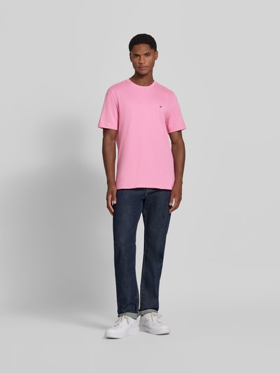 Männermodel trägt Regular Fit T-Shirt aus reiner Baumwolle von Tommy Hilfiger in Rosa, kombiniert mit Jeans, Ganzkörperansicht von vorne. Herren T-Shirt von Tommy Hilfiger