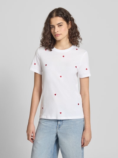 Frauenmodel trägt Regular Fit T-Shirt aus reiner Bio-Baumwolle Modell 'KETTY LIFE' von Only, unifarben mit Stickereien, Rundhals, Kurzarm, weiße glatte Baumwolle mit roten Herzapplikationen, schlichte Optik, Ganzkörperansicht von vorne.