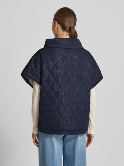 Frauenmodel trägt Cape mit Steppnähten und Eingrifftaschen von Copenhagen Muse in Dunkelblau, Relaxed-Fit, Rückenlänge 66 cm, Schulterbreite 42 cm, Brustweite 25 cm, hochgeschlossener Kragen, Knopfleiste, Ganzkörperansicht Rückansicht.