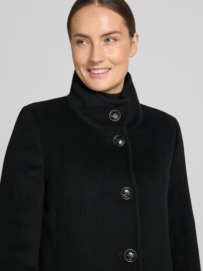 Kobiece model nosi kurtkę 'Jacke mit Stehkragen und Eingrifftaschen' od FUCHS SCHMITT, czarna, mieszanka materiałów z dodatkiem wełny, linia a, stójka, listwa guzikowa, wpuszczane kieszenie, szerokość ramion w rozmiarze 36: 37 cm, szerokość klatki piersiowej w rozmiarze 36: 48 cm, długość rękawów w rozmiarze 36: 64 cm, długość tyłu w rozmiarze 36: 73 cm, zbliżenie na górną część ciała z przodu