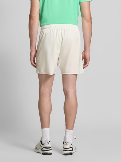 Mężczyzna nosi Regular Fit Shorts mit integriertem Slip Modell 'ICON' od ASICS TIGER, kremowy kolor, elastyczny pas, nadruk z logo, szerokość w rozmiarze M: 37 cm, długość wewnętrzna nogawki w rozmiarze M: 18 cm, widok całej sylwetki od tyłu.