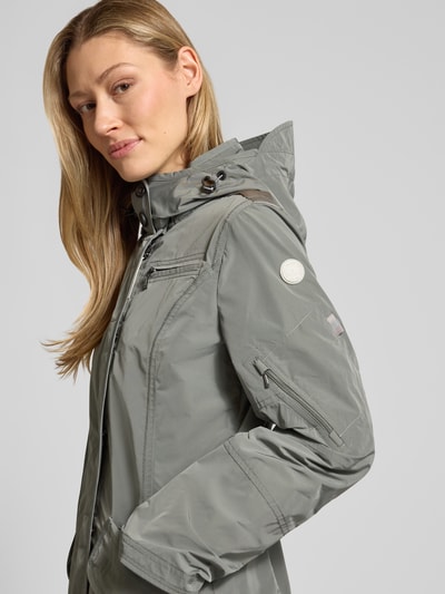 Frauenmodel trägt Jacke mit Kapuze und Pattentaschen von Gil Bret in Tailliertem Schnitt, Reißverschluss, graugrüne Farbe, Nahaufnahme Oberkörper.