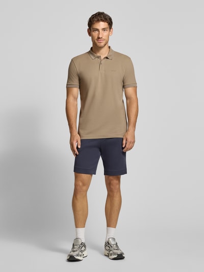 Mannenmodel draagt Regular fit poloshirt uit zuivere katoen model 'PIO 1' van BOSS Green in lichtbruin, donkere shorts, sneakers, volledige vooraanzicht.