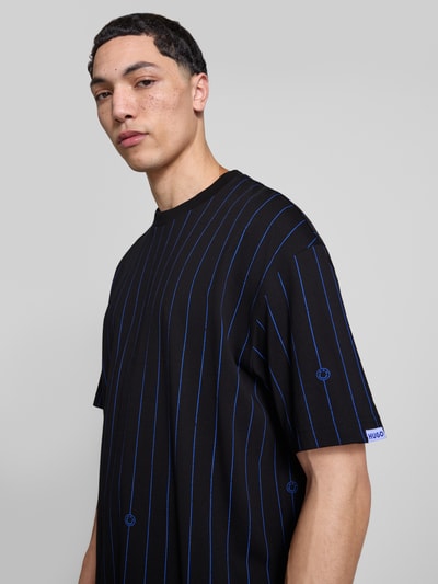 Mannelijk model draagt Regular Fit T-Shirt uit puur katoen model 'NORAYATI' van Hugo Blue, zwart met blauw gestreept allover-motief, label smiley print, ronde hals, korte mouw, jersey structuur, vooraanzicht borst-close-up.