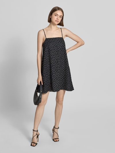 Frauenmodel trägt Minikleid im Allover-Look mit Spaghettiträgern von REVIEW aus schwarzem Satin mit weißen Punkten, A-Linie, Ganzkörperansicht von vorne. Rückenlänge bei Größe S: 70 cm, Brustweite bei Größe S: 44 cm.