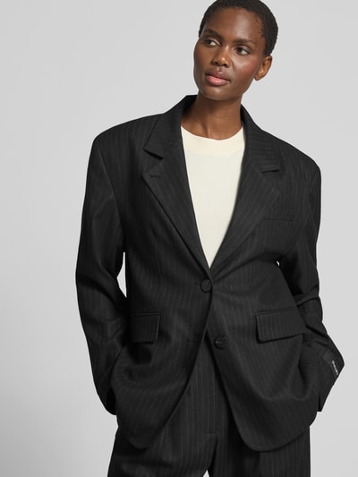 Frauenmodel trägt Relaxed Fit Blazer mit Viskose-Anteil von black palms in Schwarz mit feinem Streifenmuster, Reverskragen, 2-Knopfleiste, Logo-Patch, Elastischer-Material-Mix, Rückenlänge 76 cm, Brustweite 60 cm, Ärmellänge 66 cm, Ganzkörperansicht von vorne.