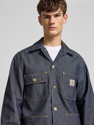 Männermodel trägt Jeansjacke mit aufgesetzten Taschen Modell 'ADEN' von Carhartt Work In Progress aus dunkelblauer Baumwolle, Nahaufnahme Oberkörper.