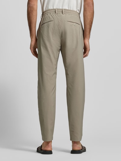 Męski model nosi Slim Fit Stoffhose mit Strukturmuster von CRUNA, elastyczna mieszanka materiałów, krój slim fit, fakturowany wzór, kieszenie z tyłu, elastyczny pas, wpuszczane kieszenie, szerokość w rozmiarze 50: 44 cm, długość wewnętrzna nogawki w rozmiarze 50: 79 cm, beżowy kolor, gładka faktura, całkowity widok z tyłu.