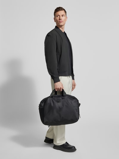Männermodel trägt schwarzen Rucksack mit Label-Detail von Emporio Armani, dezente Farben, abgerundete Form, Ganzkörperansicht von vorne. Hauptfach mit Rundum-Reißverschluss, verstellbare Schulterriemen, kurze Tragehenkel, Innenfach mit Reißverschluss, Breite 52 cm, Länge 36 cm, Tiefe 16 cm, Schulterriemen 72 cm.