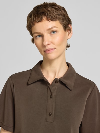 Modelka kobieca ma na sobie koszulkę polo Loose Fit Poloshirt mit kurzer Knopfleiste Modell 'Helle' od My Essential Wardrobe z mieszanki materiałów z dodatkiem wiskozy, kołnierzyk polo, krótka listwa guzikowa, długość tyłu w rozmiarze S: 57 cm, kolor brązowy, gładka faktura, ujęcie: zbliżenie górnej części ciała.