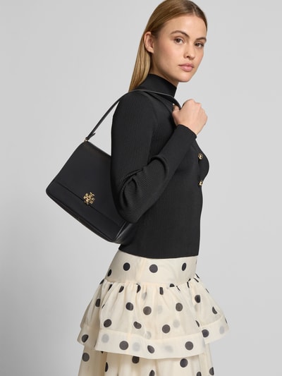Frauenmodel trägt Shoulder Bag mit Logo-Detail von Tory Burch in Schwarz, feine Struktur, goldfarbenes Logo, Überschlag, abnehmbarer Schulterriemen, Ganzkörperansicht von vorne.