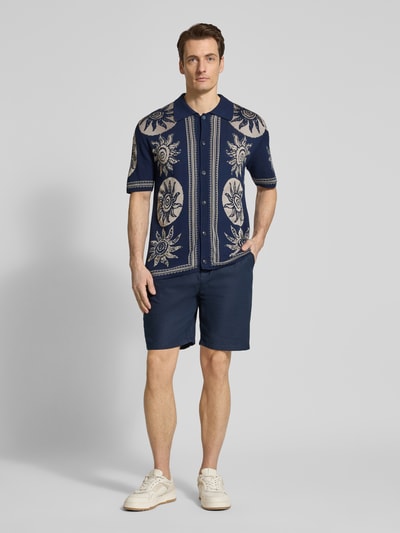 Männermodel trägt Strickshirt mit Polokragen und Knopfleiste von Scotch & Soda im Allover-Look, Baumwoll-Viskose-Mix, Regular-Fit, navy und beige Töne, Ganzkörperansicht von vorne.