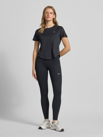 Frauenmodel trägt Damen T-Shirt mit Logo Modell 'Tempo' von NIKE TRAINING in Schwarz, Regular-Fit, Rundhalsausschnitt, Rückenlänge 56 cm, Ganzkörperansicht von vorne.