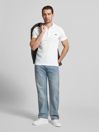 Männermodel trägt Slim Fit Poloshirt aus reiner Baumwolle von Lacoste, Optik: Unifarben, Logo-Stitching, Piqué, Ganzkörperansicht von vorne.