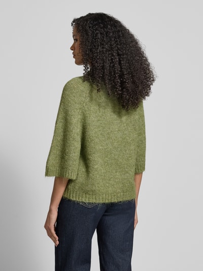 Frauenmodel trägt Strickjacke mit 1/2-Arm Modell 'Benutta Fluffy' von Neo Noir, Material-Mix mit Baumwoll-Anteil, Relaxed-Fit, grüne melierte Optik, sichtbare Grobstrick-Textur, Rundhalsausschnitt, Rückenlänge und Ärmellänge bei Größe 36 laut Kontext, Ganzkörperansicht Rückansicht.