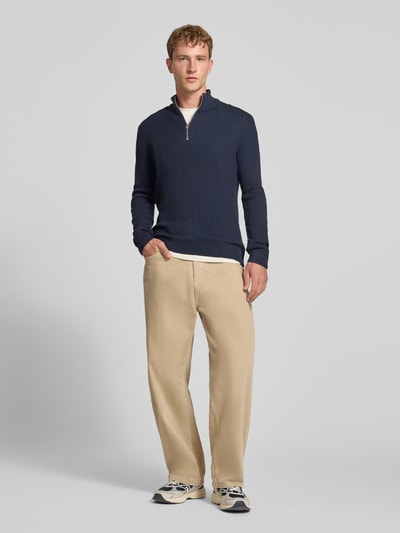 Męski model nosi sweter z dzianiny 'Strickpullover mit Troyer-Kragen Modell 'PANNEL'' od JACK & JONES, mieszanka materiałów z bawełną, dopasowany krój, długość tyłu w rozmiarze M: 70 cm, długość rękawów w rozmiarze M: 74 cm, kolor granatowy, faktura prążkowana, widok całej sylwetki z przodu.