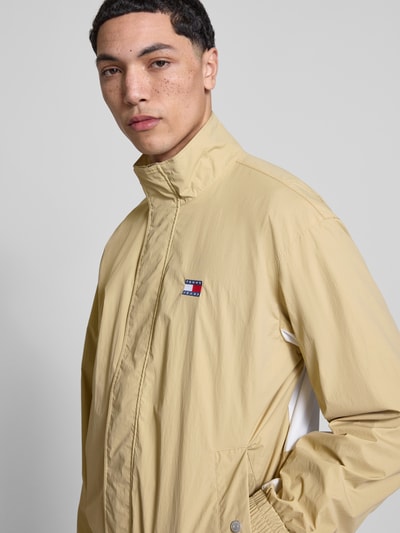 Männermodel trägt Regular Fit Blouson mit Logo-Stitching von Tommy Hilfiger in Beige mit Stehkragen und Satinstruktur, Nahaufnahme Oberkörper.