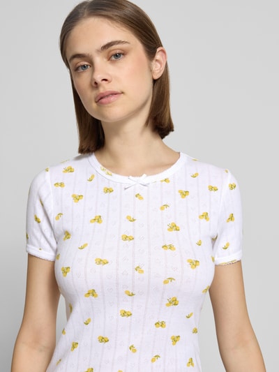 Frauenmodel trägt T-Shirt mit Schleifen-Detail Modell 'ELIZA' von JJXX, weiß mit gelbem Muster, fein strukturiert, Nahaufnahme Oberkörper. Reine Baumwolle, Regular Fit, Pointelle Strick, Rundhalsausschnitt, Rückenlänge bei Größe S: 55 cm.