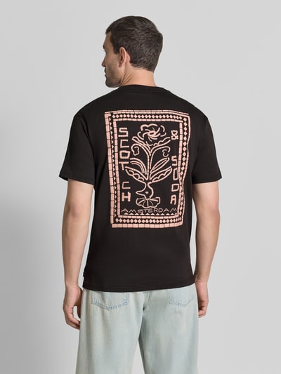 Męski model nosi T-Shirt mit Label-Print und Rundhalsausschnitt von Scotch & Soda, czarna bawełna, krój regular fit, nadruk z logo, okrągły dekolt, Długość tyłu w rozmiarze M: 72 cm, Ganzkörperansicht Rückansicht.