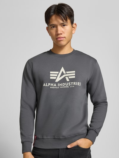 Männermodel trägt Regular Fit Sweatshirt aus Baumwoll-Mix mit Logo-Print von Alpha Industries, graue Farbe, gerippte Abschlüsse, Nahaufnahme Oberkörper.