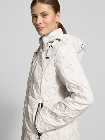 Modelka kobieca nosi Jacke mit Stehkragen und Reißverschlusstaschen od Gil Bret, biała bawełna, krój slim fit, kaptur z troczkiem, teksturowana powierzchnia, ochrona przed pogodą, zamek boczny, szerokość w rozmiarze 36: 50 cm, długość pleców: 61 cm, szerokość ramion: 37 cm, długość rękawa: 64 cm, zdjęcie z przodu w półzbliżeniu.