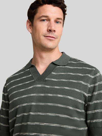 Männermodel trägt Regular Fit Poloshirt aus reiner Baumwolle von Tom Tailor in Dunkelgrün mit weißen Streifen, Nahaufnahme Oberkörper.