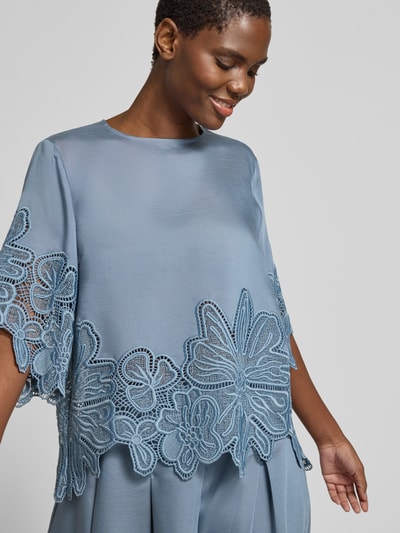 Frauenmodel trägt Blusenshirt aus Lyocell-Mix mit Spitze Modell 'MOLLY' von Copenhagen Muse in Blautönen, Relaxed-Fit, Nahaufnahme Oberkörper, Rundhalsausschnitt, florale Spitze, Rückenlänge bei Größe S: 58 cm, Ärmellänge bei Größe S: 36 cm.