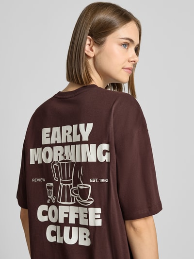 Frauenmodel trägt Oversized Fit T-Shirt aus reiner Baumwolle mit Label-Detail von REVIEW, Rückseite mit Print, dunkelbraune Farbe, Nahaufnahme Oberkörper.