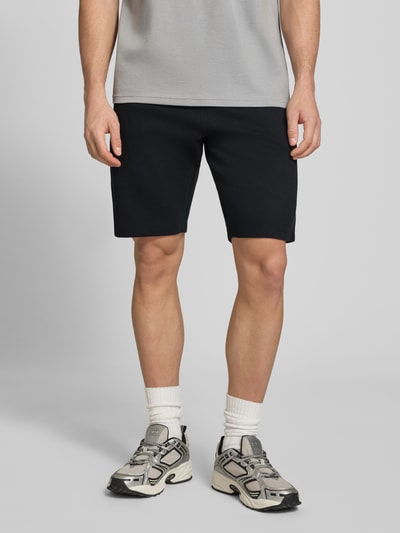 Męski model nosi Straight Fit Shorts mit Logo-Stitching Modell 'Fillip' od Blend, czarny kolor, strukturalny wzór, kieszenie z przodu i z tyłu, elastyczny pas ze sznurkiem, bawełna, Szerokość w rozmiarze M: 39 cm, długość wewnętrzna nogawki: 26 cm, zdjęcie całej sylwetki z przodu.