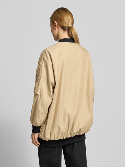 Frauenmodel trägt Relaxed Fit Jacke mit Logo-Stitching von Original Bombers in Beige mit schwarzem Saum, elastischen Abschlüssen, Rückenansicht, Ganzkörperansicht.