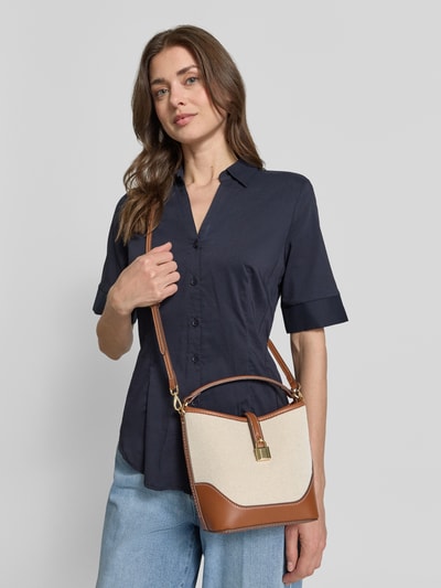 Frauenmodel trägt Bucket Bag in Flecht-Optik von Mango mit Schnallenverschluss und Schulterriemen, Beige-Braun, Ganzkörperansicht von vorne.