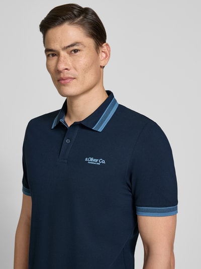 Männermodel trägt dunkelblaues Regular Fit Poloshirt aus Baumwoll-Mix von s.Oliver RED LABEL mit Label Print und Polokragen, Nahaufnahme Oberkörper.