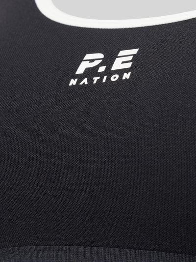 Nahaufnahme Oberkörper, Frauenmodel trägt Sport-BH mit Logo-Print Modell 'ADAPTION SEAMLESS' von P.E Nation, schwarzer Material-Mix mit weißem Logo und feiner Struktur