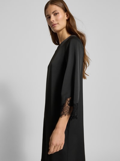 Kobiece model prezentuje sukienkę Knielanges Kleid mit Rundhalsausschnitt Modell 'Dancia' od JOOP!, czarną, z obszyciem koronką, krój relaxed fit, okrągły dekolt, długość do kolan, rękaw o dł. 3/4, widok z boku, ujęcie do pasa.