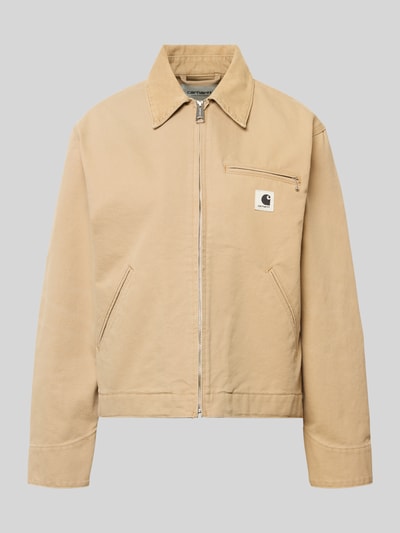 Produktfoto, Jacke mit Label-Detail von Carhartt Work In Progress aus beigefarbener Baumwolle, entspannter Schnitt, sichtbare Reißverschlüsse, Umlegekragen, schlichte Struktur.