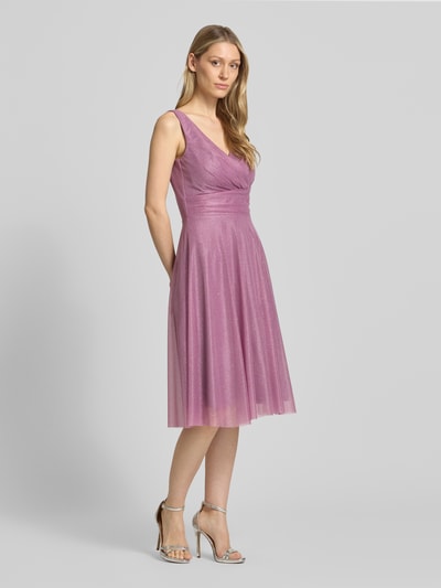 Frauenmodel trägt Knielanes Cocktailkleid mit V-Ausschnitt von TROYDEN COLLECTION in schimmerndem Mesh, taillierter Schnitt, Ganzkörperansicht von vorne. Brustweite bei Größe 36: 36 cm, Rückenlänge: 88 cm.