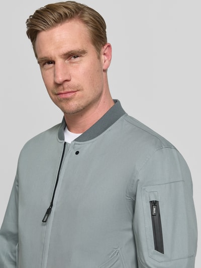 Männermodel trägt Jacke mit Stehkragen und Zweiwege-Reißverschluss Modell 'FLAP' von G-LAB aus Baumwoll-Mix, Nahaufnahme Oberkörper. Regular-Fit, dezentes Hellgrau, glatte Textur, sichtbare Nahtdetails, Maße laut Hersteller für Größe M: Rückenlänge 70 cm, Schulterbreite 53 cm, Brustweite 56 cm, Ärmellänge 66 cm.