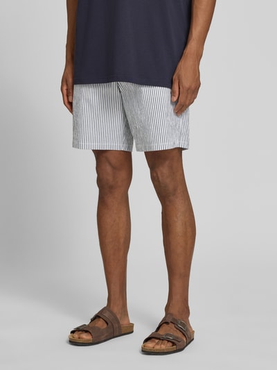 Mężczyzna nosi Regular Fit Bermudas aus Baumwoll-Mix Modell 'KARL' od SELECTED HOMME, biało-granatowe paski, tekstura seersucker, zdjęcie całej sylwetki z przodu.