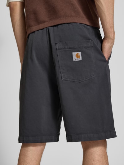 Männermodel trägt Shorts mit Gesäßtasche Modell 'Floyde' von Carhartt Work In Progress, Lyocell-Mix, Loose-Fit, dunkelgrau, Ganzkörperansicht Rückansicht.