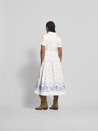 Frauenmodel trägt Hemdblusenkleid in Midilänge von Self-Portrait aus reiner Baumwolle mit taillierter Passform, Taillengürtel mit Dornschließe, Paisley-Stickereien, Länge 127 cm, Brustweite 50 cm, Ärmellänge 21 cm, Taillenweite 55 cm, cremeweiß mit hellblauem Muster, glatte Textur, Ganzkörperansicht Rückansicht.