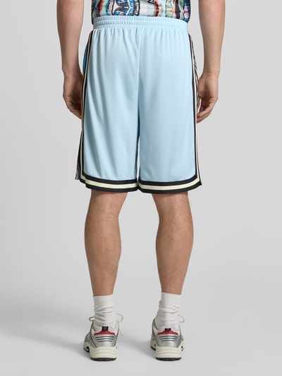 Męski model nosi Shorts aus Mesh mit Kontraststreifen von COLUCCI w jasnoniebieskim kolorze, prosty krój, elastyczny pas, kontrastowe paski, szerokość w rozmiarze M: 37 cm, długość wewnętrzna nogawki: 24 cm, widok całej sylwetki od tyłu.