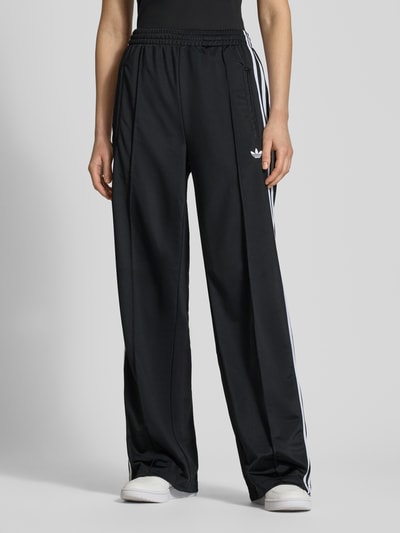 Frauenmodel trägt Sweatpants mit elastischem Bund von adidas Originals in Schwarz, Lockerer-Schnitt, Reißverschlusstaschen, Label-Stitching, Ganzkörperansicht von vorne. Innenbeinlänge bei Größe S: 79 cm.